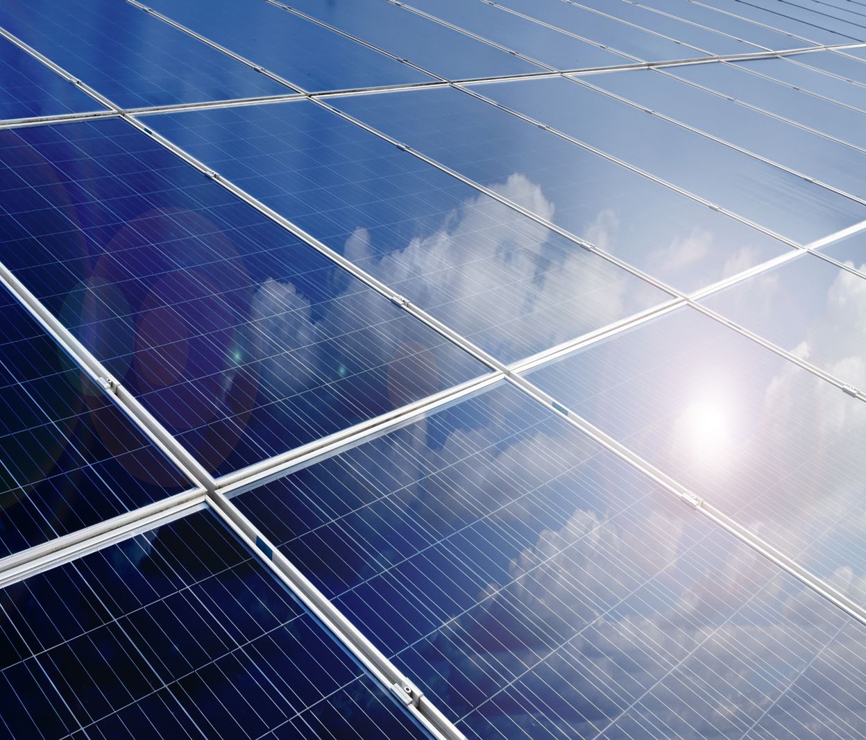 Nahaufnahme von Solarpaneelen, die den blauen Himmel mit weißen Wolken und Sonnenstrahlen reflektieren
